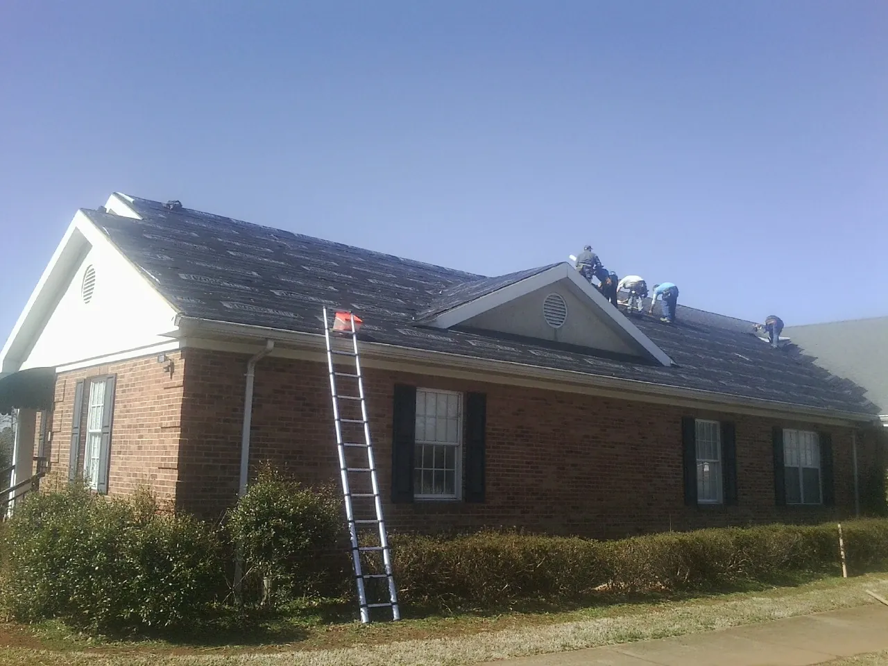 Crew tearing shingles off a brick ranch roof with a ladder set — Emergency Roof Repair work by our crew in Ridgeway