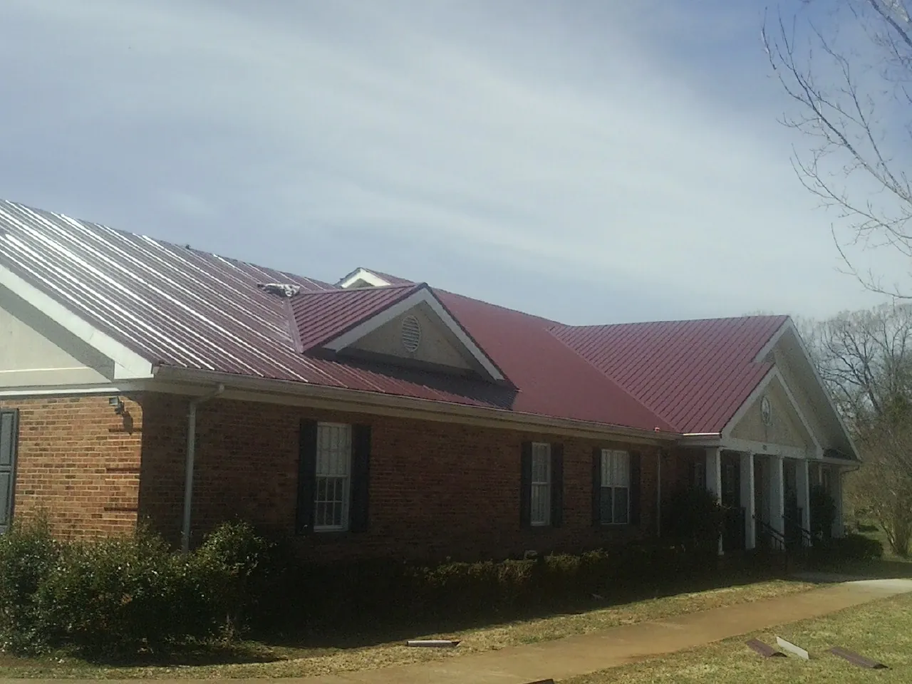 Red metal roof with gabled entries on a long brick building, from a Hail Damage Roof Repair job in Ridgeway